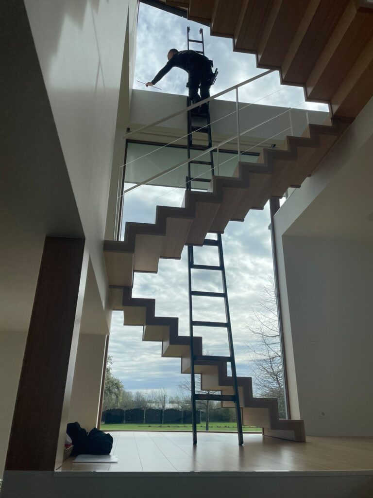 Persoon op ladder bij moderne houten trap in lichte ruimte met grote ramen